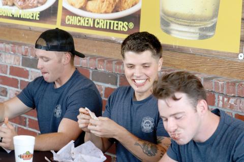 Live Oak firefighter Zach Yarnell (center) grins as Cody Byers (right) has a mouthful of ribs during the contest Tuesday. Kessler Mallory (left) also participated for the Live Oak Fire Department team. (TONY BRITT/Lake City Reporter)