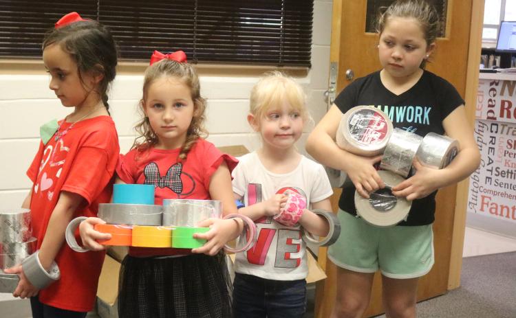 Eastside Elementary School students Ryleigh Trespalacios (from left), Aunna Hartopp, Summer Bedenbaugh and Ariana French bring rolls of duct tape to the school library Thursday morning. The school hopes to set a world record for the largest ball of tape. (TONY BRITT/Lake City Reporter)