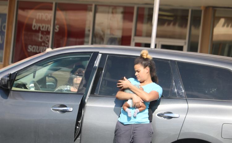 The woman authorities say left a baby unattended in a car Monday afternoon sits in the vehicle at Lake City Plaza as the baby’s mother holds the child. (TONY BRITT/Lake City Reporter)