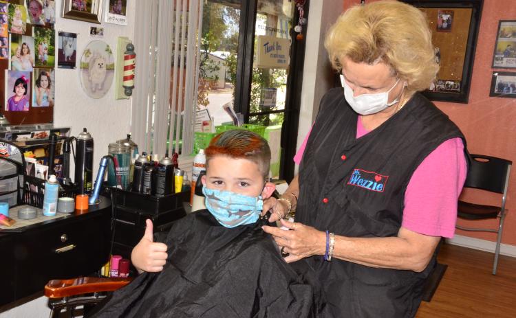 Louise Huelskamp, better known as “Miss Wezzie,” puts the finishing touches on 8-year-old Hagan Stalvey, who also asked for a touch of pink coloring in his hair.         As the state continues relaxing quarantine restrictions, hair salons and barber shops were allowed to reopen on Monday. (CARL MCKINNEY/Lake City Reporter)