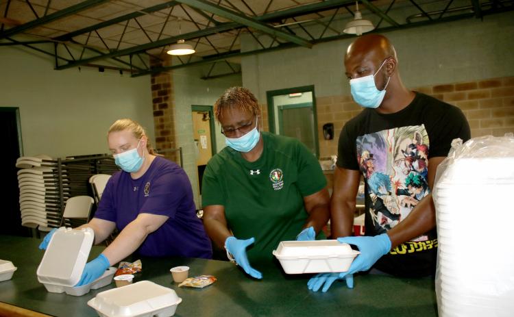 Columbia County Recreation Department employees Courtney Rowe (from left), Lynda Caldwell and Chad Owens practice preparing and distributing meals in the Richardson Community Center cafeteria Thursday afternoon. (TONY BRITT/Lake City Reporter)