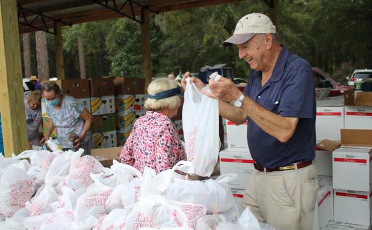 Bud Parker works on tying a plastic bag as he and other volunteers at Lake City Church of Christ distribute food and other commodities Thursday afternoon. More than 200 vehicles passed through the event collecting bags and boxes of food. (TONY BRITT/Lake City Reporter)