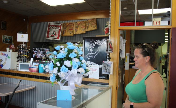 Caryn Cooper, daughter of the late Robert Warren Cooper Jr., who was the owner of the Pizza Boy Pizza restaurant, looks at a bouquet of flowers on the restaurant’s counter Wednesday afternoon. (TONY BRITT/Lake City Reporter)