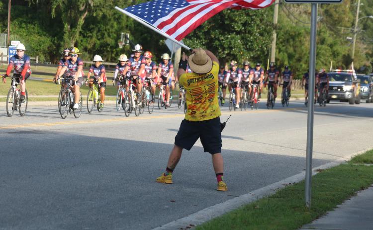 Zak Jones with the North Collier Fire Department waves an American flag Wednesday evening as dozens of Brotherhood Ride cyclists end their week-long trek across Florida at the Live Oak Fire Department station. The Brotherhood Ride is an annual bike ride to honor first responders who died in service. Former Suwannee County Fire Chief James Sommers was among those honored this year. Sommers died in August 2019. (JAMIE WACHTER/Lake City Reporter)