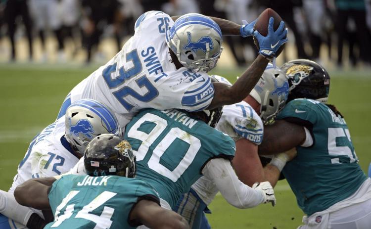 Detroit Lions running back D'Andre Swift (32) leaps over Jacksonville Jaguars linebacker Myles Jack (44) and defensive tackle Taven Bryan (90) for a touchdown on Oct. 18 in Jacksonville. (PHELAN M. EBENHACK/Associated Press))