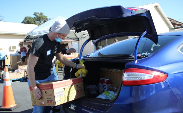 Jared Fraze, a Covenant Community School student, puts bags of food into a client’s car during Thursday’s Catholic Charities Thanksgiving basket giveaway. (TONY BRITT/Lake City Reporter)