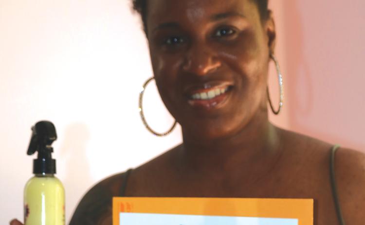 Shanekia Bing holds up one of her products along with a page from her U.S. trademark for her hair product line. (JAMIE WACHTER/Lake City Reporter)