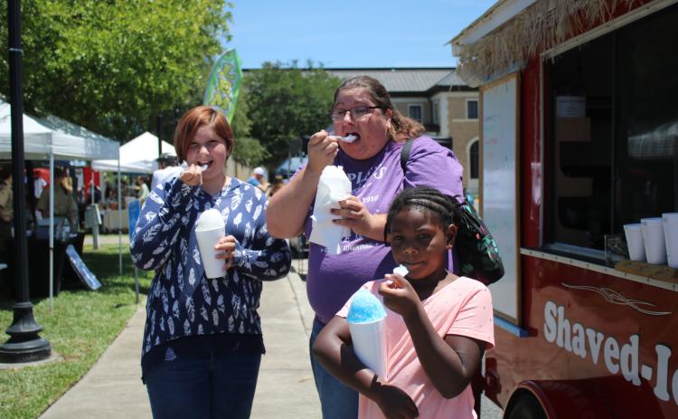 Hannah Hunter (from left), Jessica Frame and Kaleah Shead enjoy their cups of shaved ice while attending the Spring Market in Olustee Park on Saturday. (TONY BRITT/Lake City Reporter)