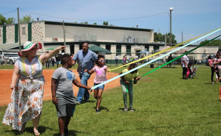 Elana Ramos (from left) points out to JaMarian Lane to watch how the ribbons are getting platted on the May Day pole during a NorthStar Family Resource Center May Celebration Saturday afternoon at Richardson Community Center. (TONY BRITT/Lake City Reporter)