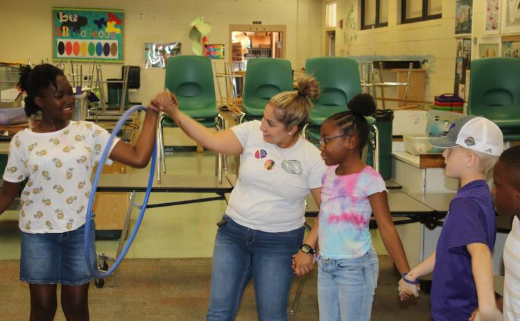 An unidentified child is passed a hula hoop from Columbia County Sheriff’s Office School Resource Deputy Nicole Martell during an activity during camp Tuesday. (TONY BRITT/Lake City Reporter)