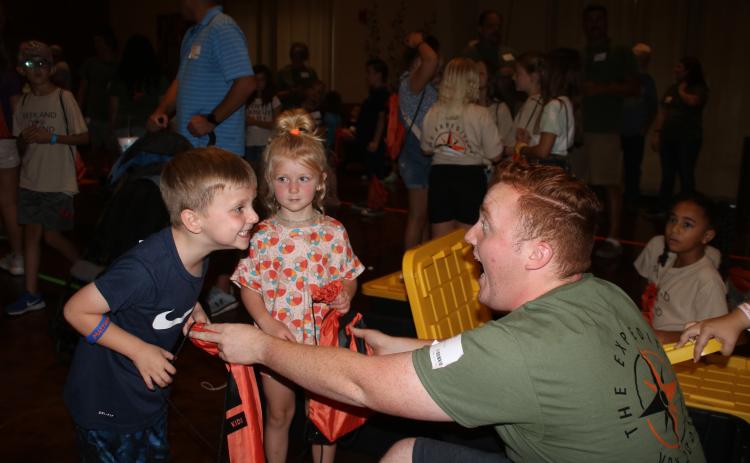 Easton Helsel (left), 5, makes a face with Jacob English (far right) during the Christ Central Vacation Bible School session Wednesday night as Emery Helsel, 4, looks on while English gives them drawstring book bags. (TONY BRITT/Lake City Reporter)
