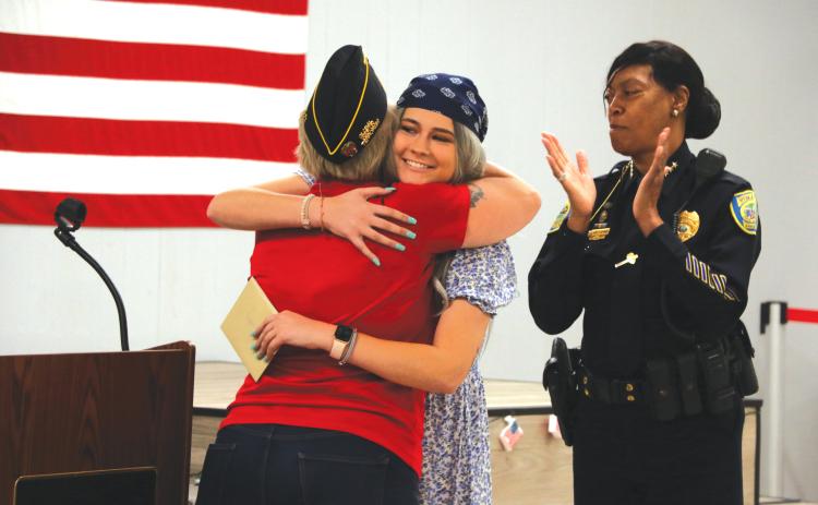 Taylor Sapp (middle) hugs 3rd Vice Commander of American Legion Post 57 Victoria Ziegler as Lake City Police Chief Argatha Gilmore offers applause Tuesday night. (MORGAN MCMULLEN)