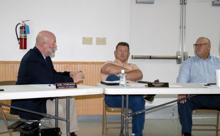 County Attorney Joel Foreman, left, reads the county charter off his phone Thursday after officials were informed their meetings in Fort White may be in violation. County Commissioners Tim Murphy, center, and Rocky Ford listen. (TONY BRITT/Lake City Reporter)