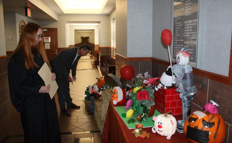 Several decorated pumpkins, including one that resembles Pennywise the Dancing Clown from the movie ‘It,’ sit in the lobby of the Columbia County Courthouse as Columbia County Judge Sara Carter (left) and Columbia County Clerk of Courts Jay Swisher examine entries. (TONY BRITT/Lake City Reporter)
