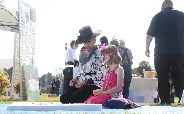 Dulcinea Strube (left) teaches 7-year-old Olivia Carr how to play jacks near the Woman’s Club setup Saturday during Founder’s Day celebrations. (MORGAN MCMULLEN/Lake City Reporter)