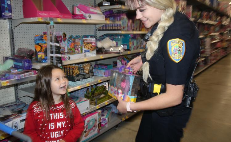 Sarah Yaun, 6, gives a grin to Lake City Police Officer Taylor Sapp as the two look at a Lil dippers Neon fish tank during the LCPD Shop with a Cop event Wednesday morning at Walmart. Local police officers took 26 children shopping for Christmas gifts. (TONY BRITT/Lake City Reporter)