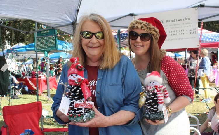 Janice Medford (left) and Jaime Brock show off snowmen made out of pinecones at a vendor’s booth on Saturday. (TONY BRITT/Lake City Reporter)