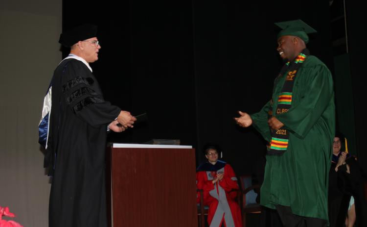 A Florida Gateway College graduate walks across the stage Friday during a commencement ceremony to receive his degree from Brian Dopson, the college’s vice president of academic affairs. FGC hosted the first two of four graduation ceremonies Friday, the other two are scheduled for Monday. (TONY BRITT/Lake City Reporter)