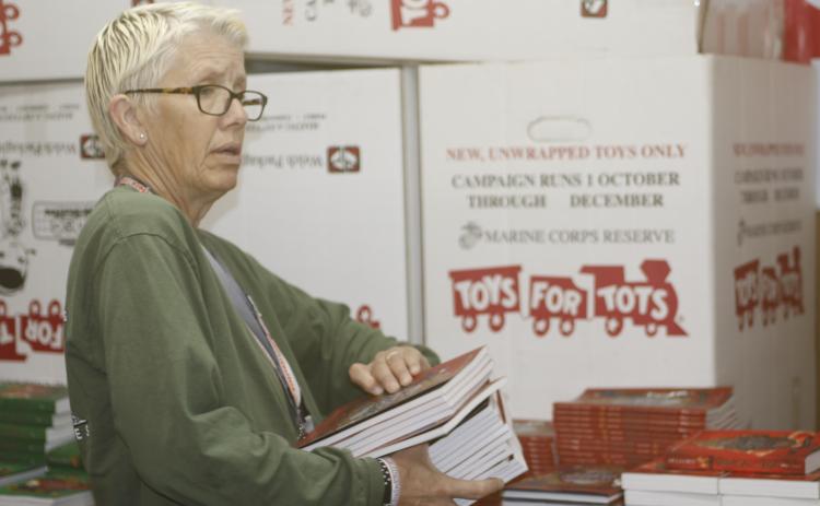 Inga Dwyer, the Toys for Tots coordinator for Columbia and Suwannee counties, helps load a stack of books Thursday for the Lake City Christian Academy. Dwyer used leftover funds to provide books for local schools during Literacy Month. (JAMIE WACHTER/Lake City Reporter)