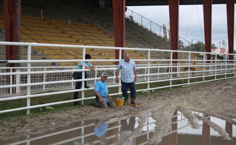 Dale Brown (middle) and Terry Hayes get muddy while working on verifying stakes that will be used for timers during the 28th Aannual Florida Gateway Pro Rodeo in the Florida Gateway Fairgrounds Rodeo Arena on Thursday afternoon. Kylee Brown (left) looks on. (TONY BRITT/Lake City Reporter)