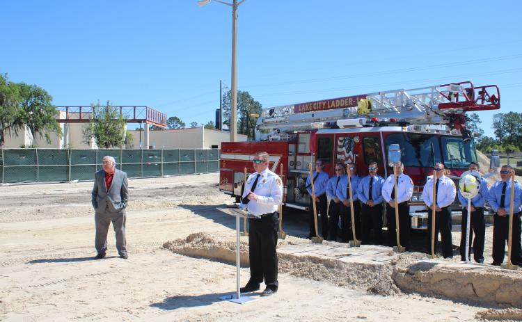 Stephen Witt (far left) looks on as Josh Wehinger, Lake City Fire Department Chief, addresses the audience during a groundbreaking ceremony for Lake City Fire Station 2 with a group of firefighters in the background.