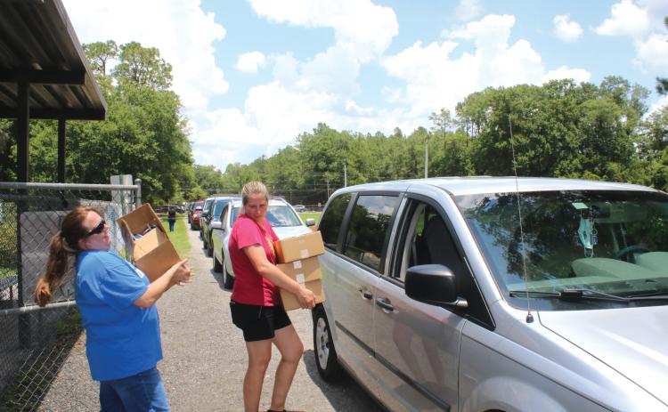 Alicia Blackford (from left) and Laurie Renegar carry meals to a minivan at Five Points Elementary School last summer. (FILE)