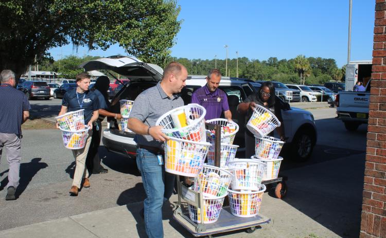 Trent Linn (from left), Lake City Correctional Facility Core Civic business manager, Daniel Taylor, Columbia High School principal Trey Hosford and Sonical Mitchell, local “baskets of love” onto trailers Thursday morning at Columbia High School. (TONY BRITT/Lake City Reporter)