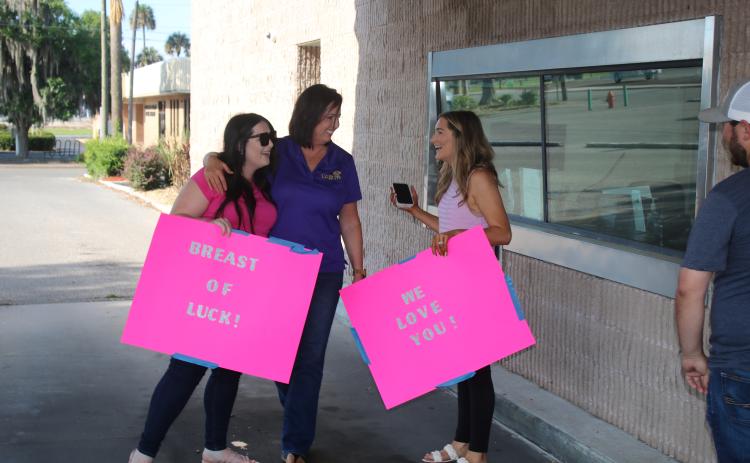 Amy Byrd (center) gets a hub and shares a laugh with her daughters Alexis Collins (left) and Leigh-Anna Boone. Collins and Boone showed up at city hall with posters of support for their mother and to watch the parade of city vehicles supporting her in her fight against breast cancer. (TONY BRITT/Lake City Reporter)