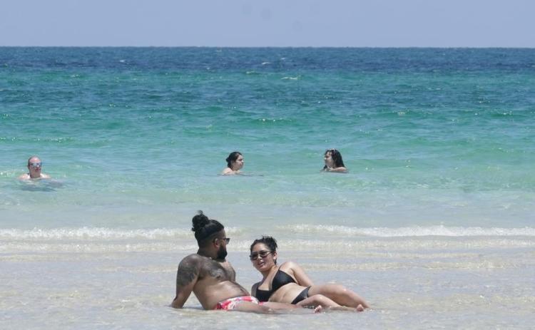 A couple sun bathes on a sand bar July 13 in Miami Beach. (MARTA LAVANDIER/Associated Press)