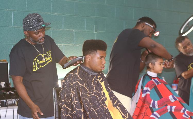 Tyrone Mullins (standing), an organizer for the Community Barbers Giving Back event, works as one of 11 barbers on Sunday that provided free haircuts at the back to school event. (TONY BRITT/Lake City Reporter)