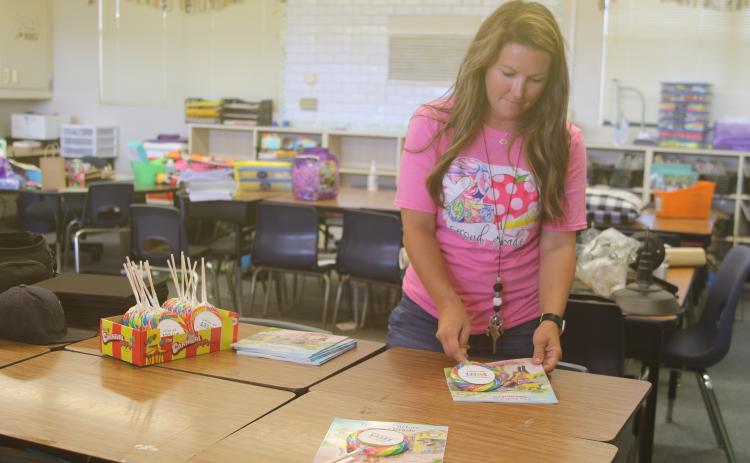 Amber Thomas, an Eastside Elementary School second grade teacher, sets a lollipop and book on desks Wednesday. (TONY BRITT/Lake City Reporter)