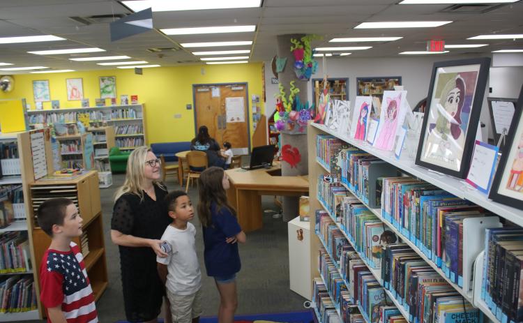 Tracy Mitchell (black dress), Alexander Mitchell, 8, (gray shirt), Isaac Gollery, 10, (red/white/blue shirt) and Audrey Mitchell, 10, (blue shirt) look at youth-submitted art pieces in the Columbia County Public Library on Thursday afternoon. The pieces, which will be on display at the library throughout September, are pieces that were submitted for the Third Annual Columbia County Public Library Youth Art Contest. (TONY BRITT/Lake City Reporter)