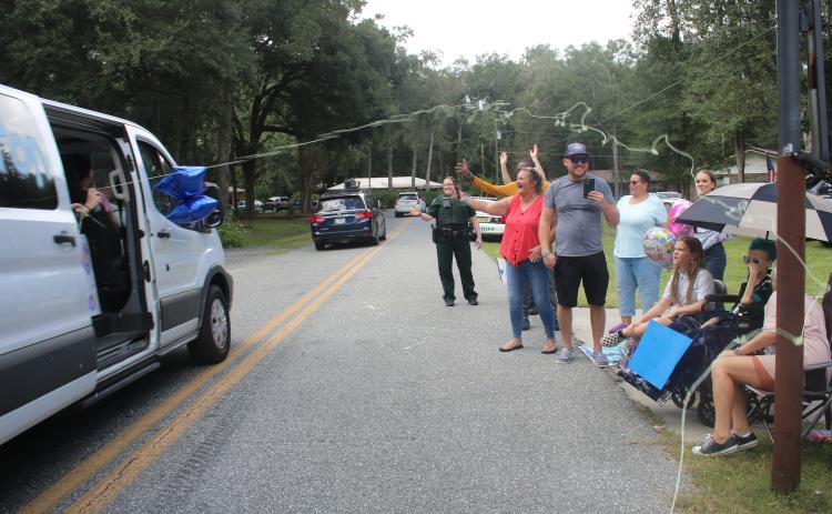 Belmont Academy students shoot silly string out of a van at Peyton Hamilton (under umbrella) and her family members during Monday’s parade. (TONY BRITT/Lake City Reporter)