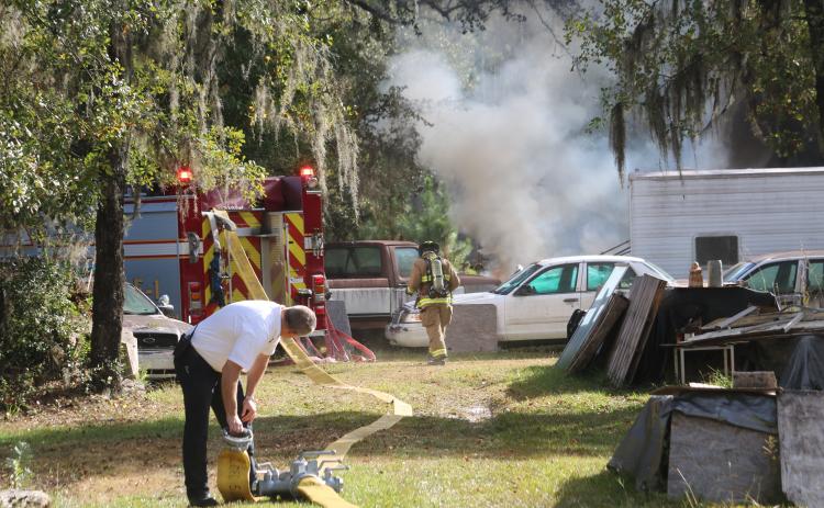 Dwight Boozer, Assistant Fire Chief of the Lake City Fire Department, looks over this shoulder while coupling hoses as a firefighter heads toward the blaze in the background. (TONY BRITT/Lake City Reporter)