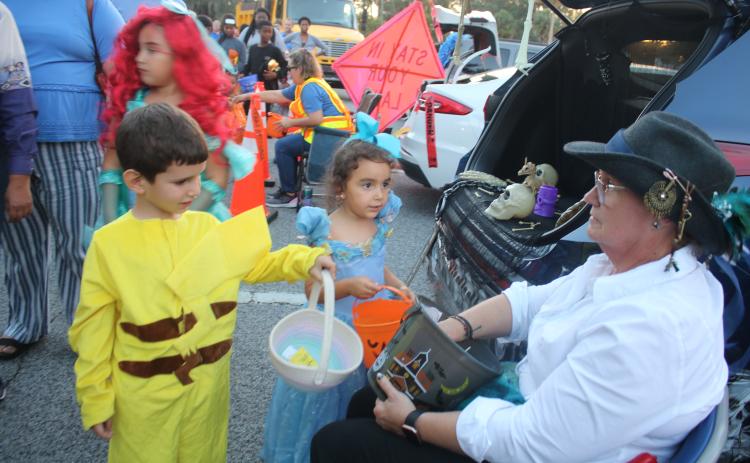 Omar Orta (from left), 4, and Adeline Garcia, 4, get candy from DOT employee Karen Williams on Monday evening at the inaugural FDOT Trunk or Treat event. (TONY BRITT/Lake City Reporter)