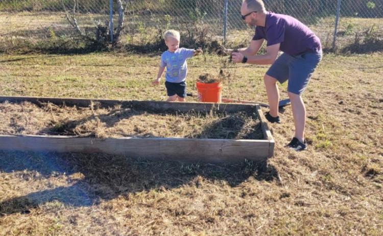 A volunteer plays with a child as they work toward building out a raised plant bed at Richardson Community Center Saturday. (COURTESY)