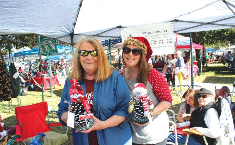 Janice Medford (left) and Jaime Brock show off snowmen made out of pinecones at a vendor’s booth during last year’s holiday market. (FILE)