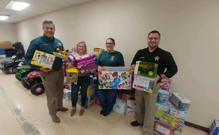 Columbia County Sheriff Mark Hunter (from left) stands with other sheriff’s office employees Paige Milligan, Sarah Wheeler, and Sgt. Chris Parker as they show toys that were purchased and donated from the agency’s inaugural ‘Deputy Clause for a Cause’ program. (TONY BRITT/Lake City Reporter)
