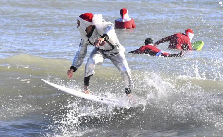Surfer Corey Howell in a space man Surfing Santa suit, rides with waves with other surfing Santas for the 14th annual Surfing Santas of Cocoa Beach event Christmas Eve morning, Saturday, Dec. 24, 2022. Cold temperatures in the 30s Fahrenheit thinned out the surfers, but thousands showed up for the annual holiday event that benefits the Florida Surf Museum and Grind for Life, a local charity benefiting people with cancer. (MALCOLM DENEMARK/Florida Today via AP)