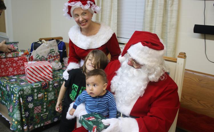 Ilyas Rosado, 10 months, sits on Santa’s lap as Ryatt Rosado, 7, poses for a picture with Ms. Claus on Friday evening during the Cookies With Santa event. (TONY BRITT/Lake City Reporter)
