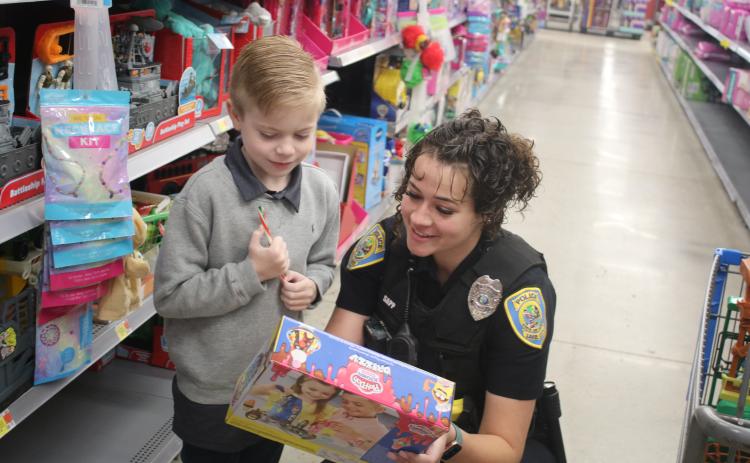 Dexter Gamble, 7, and Lake City police officer Taylor Sapp, look at the specs on a toy Gamble was considering purchasing during the Shop With A Cop event on Wednesday morning at Walmart. The Lake City Police Department has hosted the event for 10 years. (TONY BRITT/Lake City Reporter)