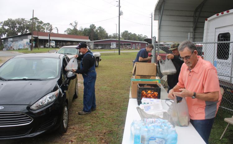Cy Perkins (far left) gives a meal to a visitor at the Parkview Baptist Church parking lot on Thursday morning as Paul Tomassini and Ricky Beauchamp prepare other meals during the Mt. Caramel Baptist Church’s ‘Feed My Lambs’ community outreach program. (TONY BRITT/Lake City Reporter)