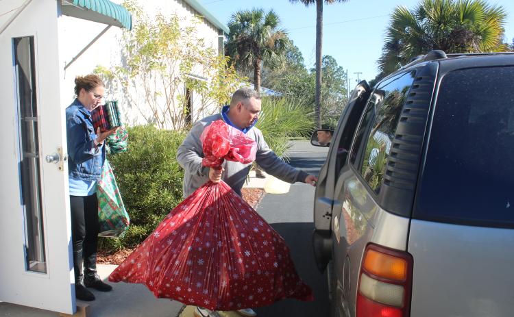JD Curls prepares to load a bag of toys into a vehicle as Jennifer Davis brings a handful books and other items to the vehicle during the Christmas basket dispersal Monday morning at the Christian Service Center. (TONY BRITT/Lake City Reporter)