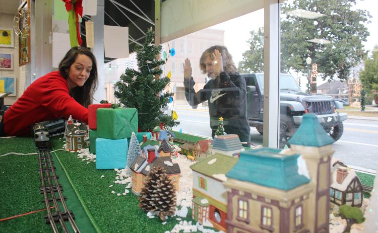 Shane McPherson, 13, of Gainesville, peers through the Gateway Art Gallery window Wednesday as his aunt, Shelia Carr, Gateway Art Gallery curator, works on a holiday display that features a holiday village with a working electric train. (TONY BRITT/Lake City Reporter)