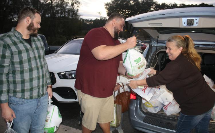 Josh Fuller (from left) and James Crenshaw pass turkeys to Dawn Johnson for the Elks Lodge Christmas baskets Thursday night. (TONY BRITT/Lake City Reporter)