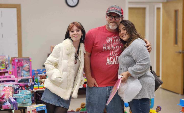 Kids Feeding Kids officials Emily Cole (from left), John Cole and Sharon Simpkins share a group hug during the organization’s ‘Miracle on KFK Street’ on Saturday night. (COURTESY)