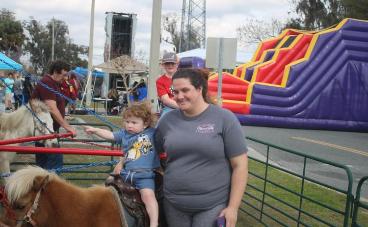 West-Lynn Eversole, 18 months, is secured to a pony by Doris Whitehead as Landon Green, 8, follows on the next pony at a vendor ride during opening day activities for the 44th Annual Olustee Festival which took place in Wilson Park adjacent to Lake DeSoto. The festival continues this morning  with a 5K race, Fun Run and vendors opening and performers beginning entertainment at 9 a.m. (TONY BRITT/Lake City Reporter)