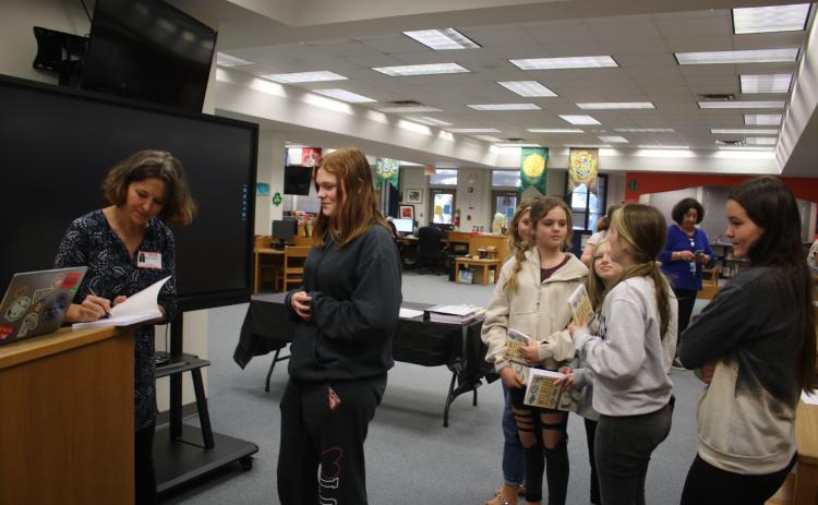 Sandra Poucher (from left) autographs a copy of her book, ‘Wildlife of Florida’s Springs,’ for Sanafa Sanders on Monday morning in the Fort White High School Media Center. (TONY BRITT/Lake City Reporter)