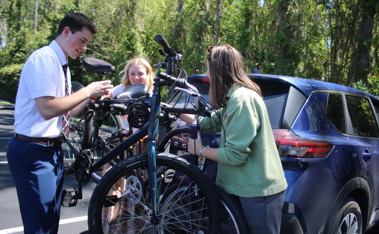 Elder Carter Snow (from left) helps Sisters Kimberlie Palmer and Tara Wallace secure their bikes on a bicycle rack on Thursday afternoon in the Church of Jesus Christ of Latter Day Saints parking lot on Old Country Club Road. The missionaries were taking part in Transfer Day where they were pairing-up with new companions to conduct their mission work. (TONY BRITT/Lake City Reporter)