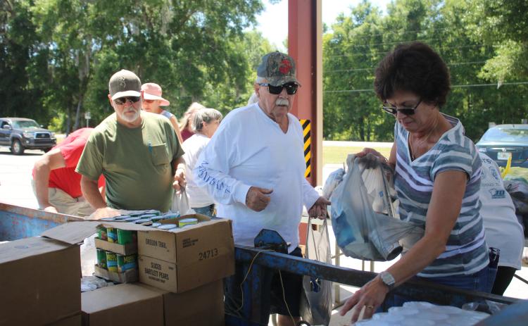 Mark Nelson (from left) and Bill Cooper wait in line as Tina Scavetta collects different canned foods while preparing food bags that will be given to local residents. Cooper, Nelson and Scavetta are volunteers supporting the North Central Florida Young Marines food distributions in Fort White. (TONY BRITT/Lake City Reporter)